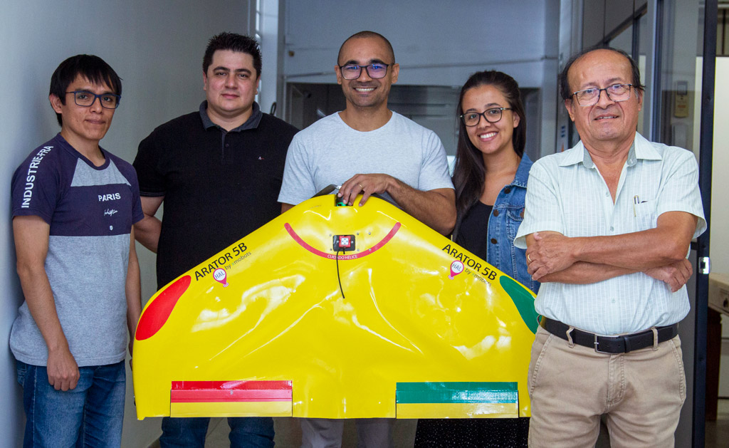 um grupo de pessoas posando junto a um drone amarelo.