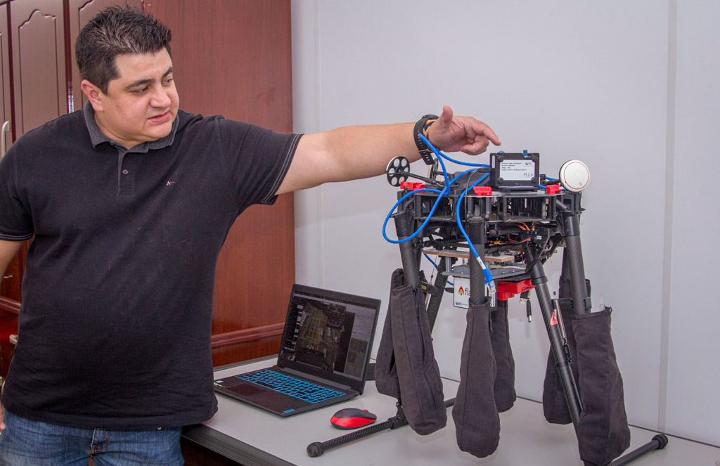 Um homem demonstrando um drone que está sobre uma mesa.