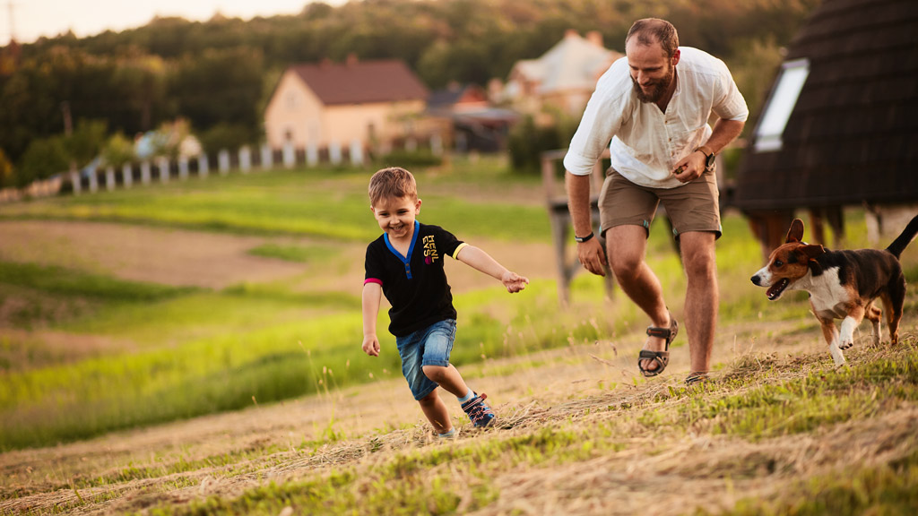 Pai, filho e cachorro brincando no campo.