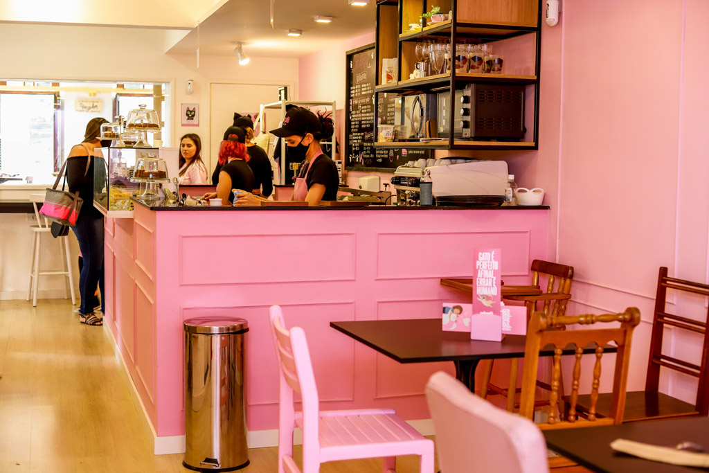 Um balcão rosa e algumas mesas dentro de uma cafeteria