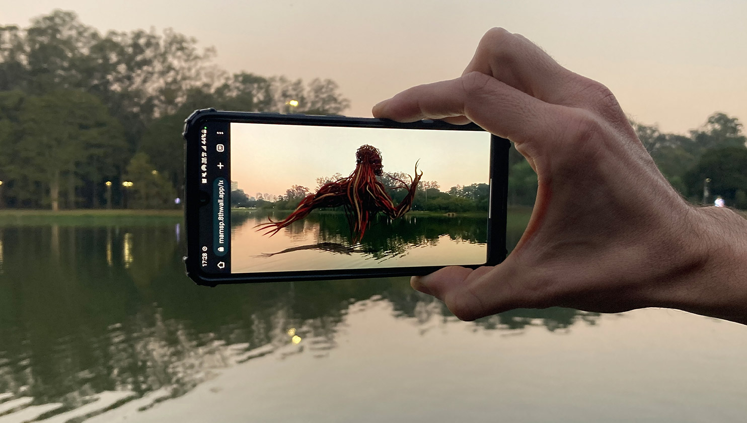 Uma mão segurando um celular utilizando realidade aumentada apontado para um lago