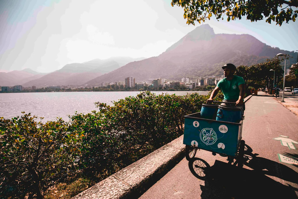 Um homem pedala uma bicicleta de carga transportando barris de compostagem.