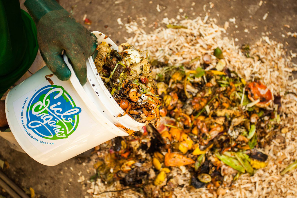 Uma pessoa vertendo um balde com resíduos orgânicos em uma composteira.