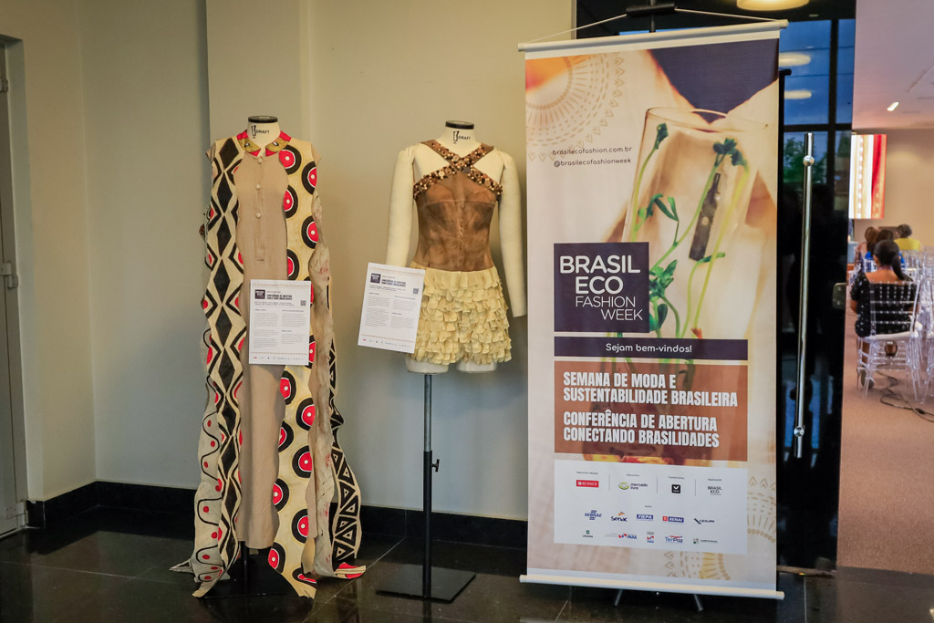Dois manequins exibindo roupas e um banner do evento Brasil Eco Fashion Week.