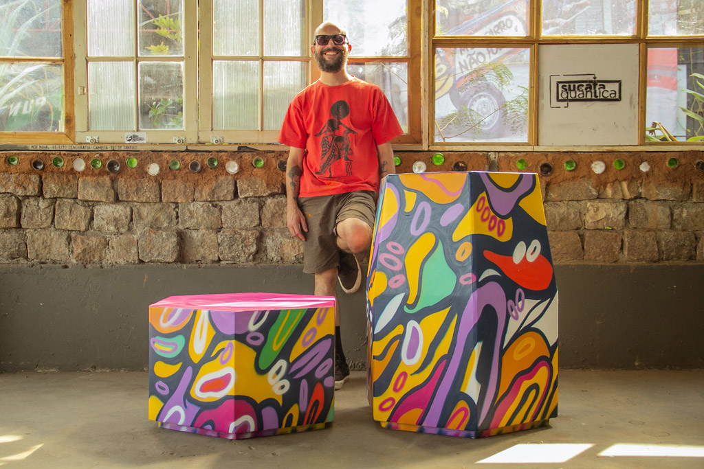 Um homem sorridente ao lado de duas caixas com pinturas coloridas abstratas.