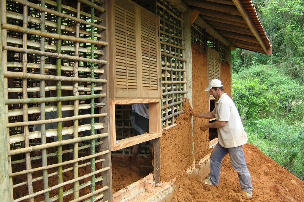 Um pedreiro trabalhando no reboco de uma bioconstrução;