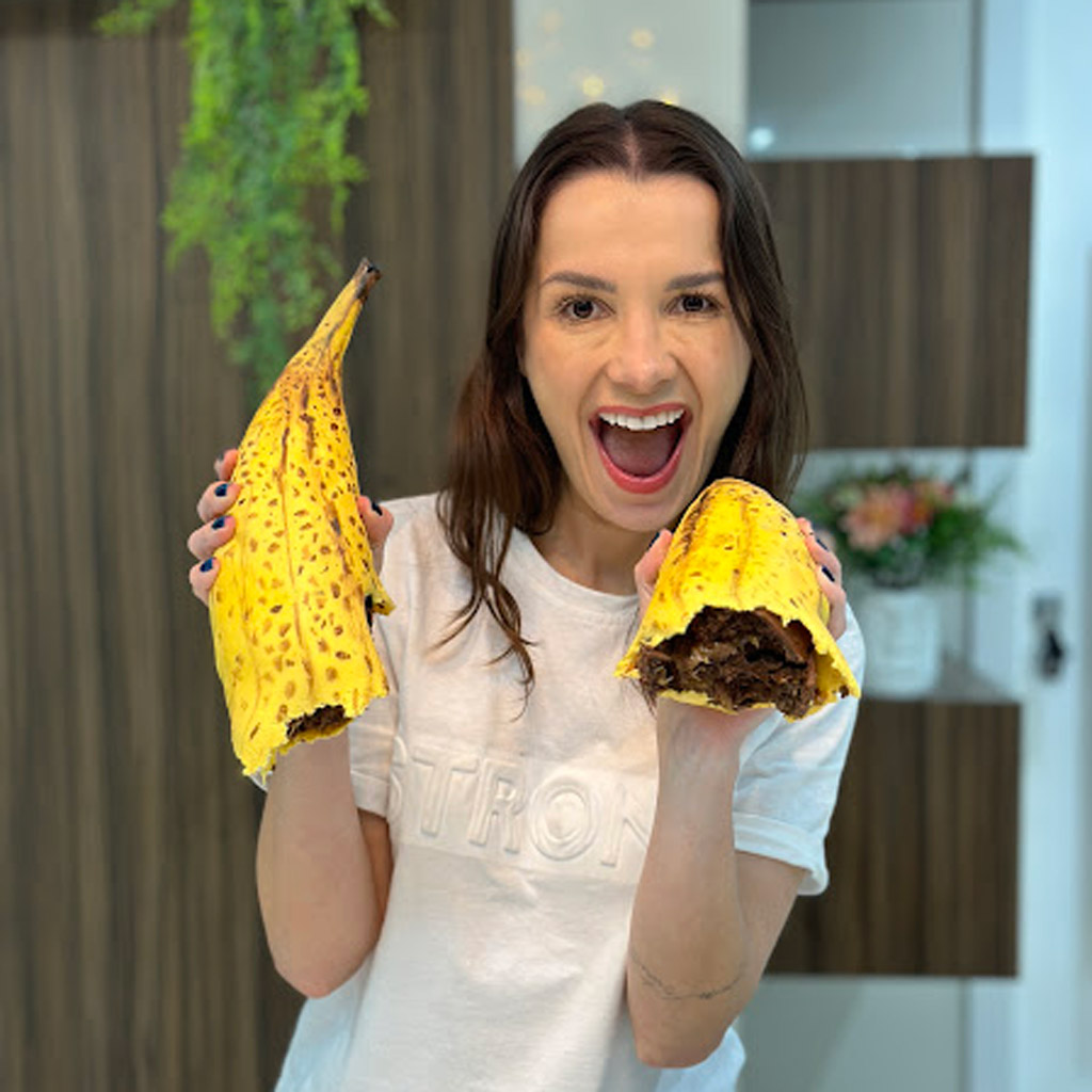 Uma mulher sorridente segurando um bolo realista em formato de banana