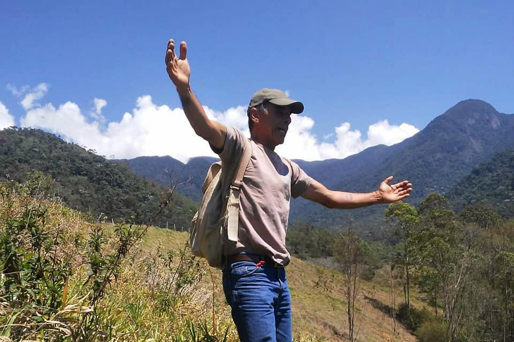Um homem com os braços abertos em uma paisagem montanhosa.